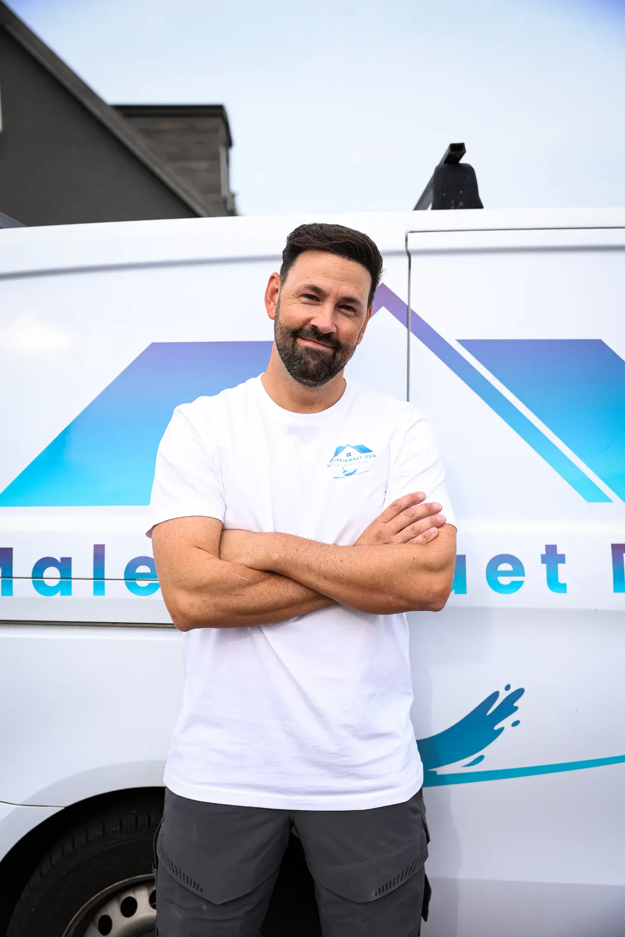Maler med armene krydsede foran malerfirmaets varevogn.
