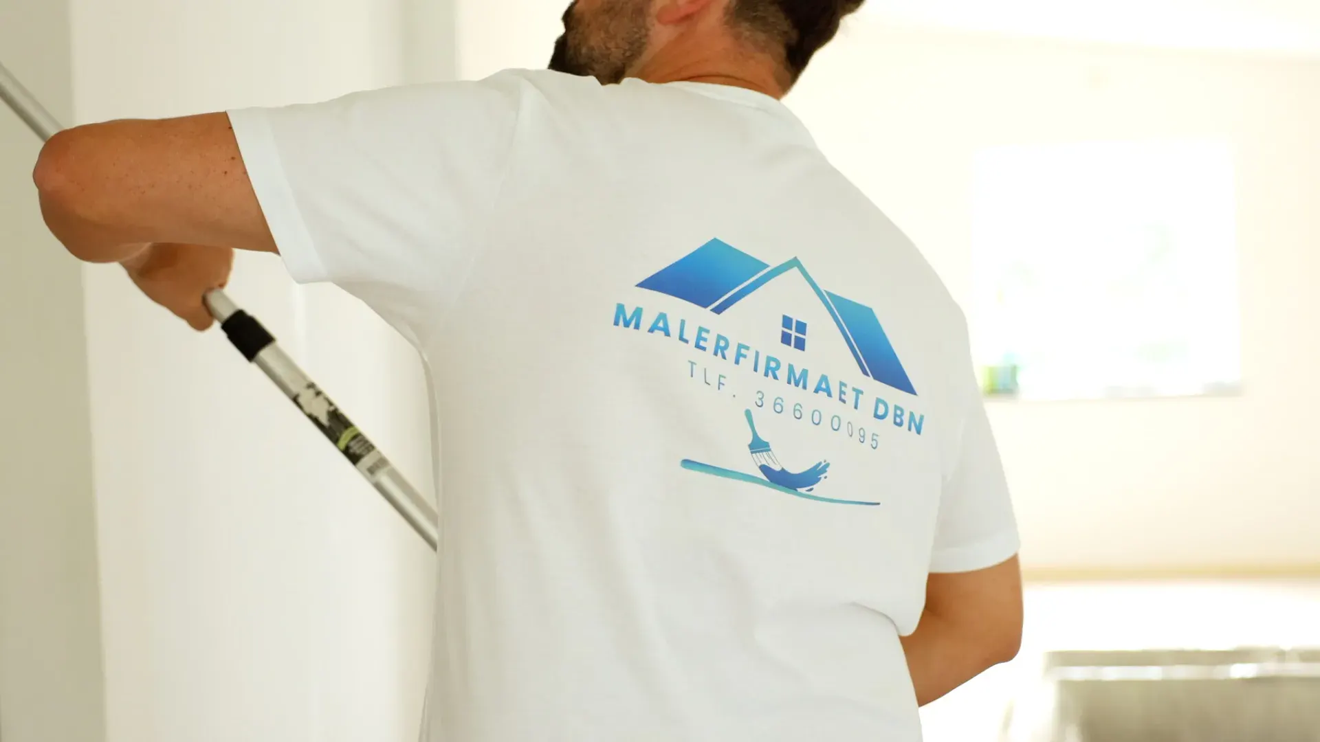 Maler arbejder med vægmaleri i et lyst rum.